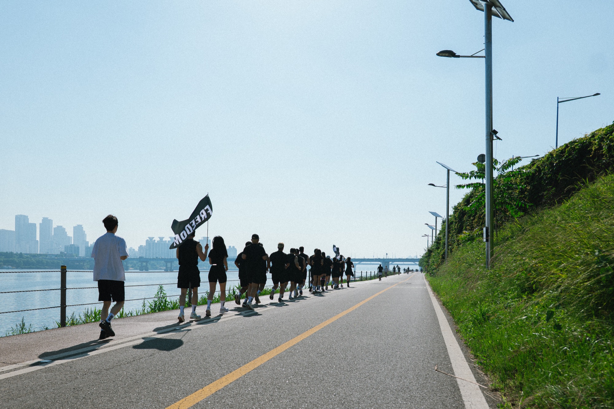 프리덤 크루가 한강 자전거 도로에서 FREEDOM 깃발을 들고 대열을 이뤄 러닝하는 장면