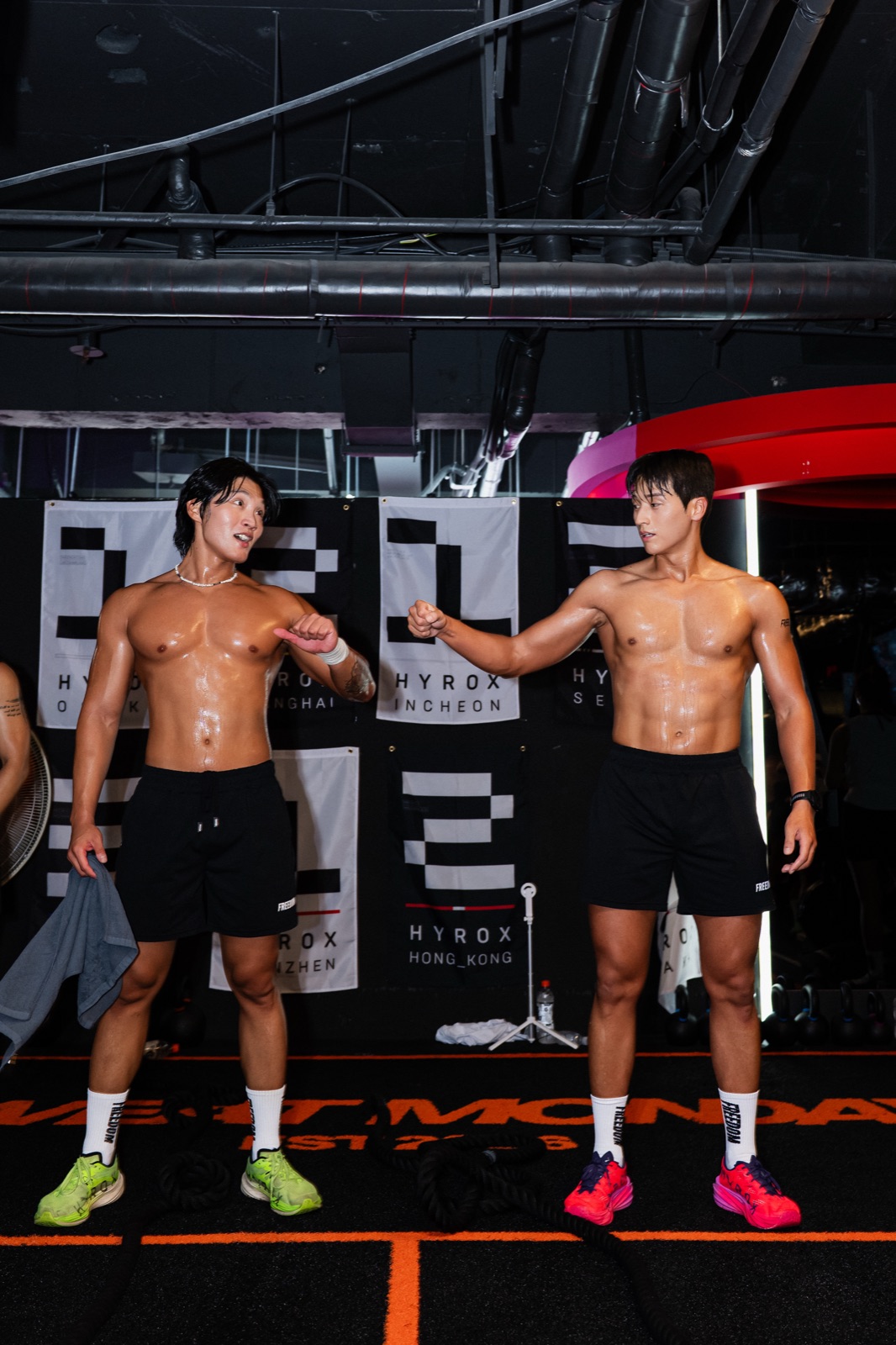 Two athletes fist-bumping in front of HYROX city banners after the set