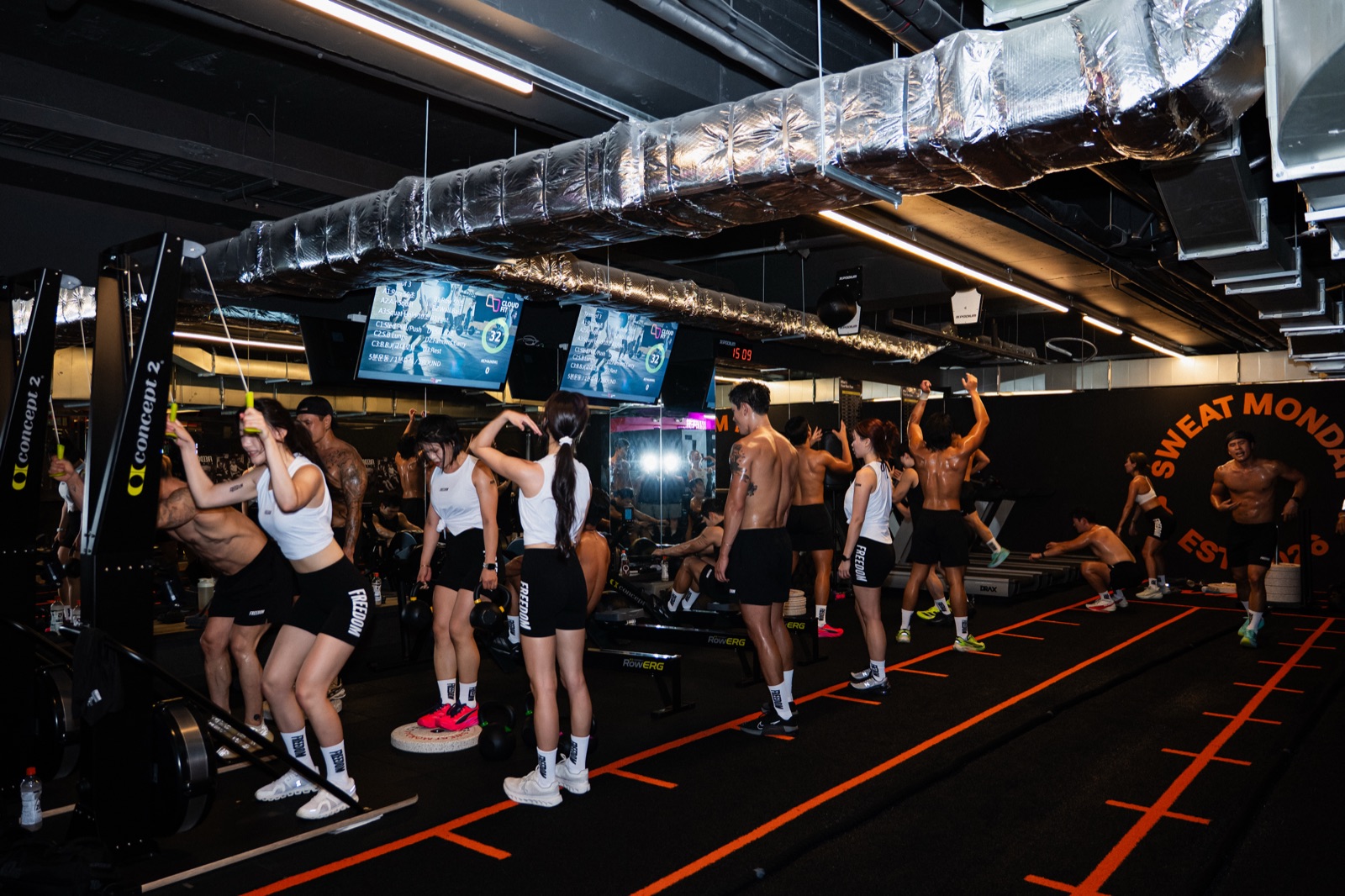 Wide shot of the SWEAT MONDAY training floor — kettlebells, RowErg and treadmills running as one circuit